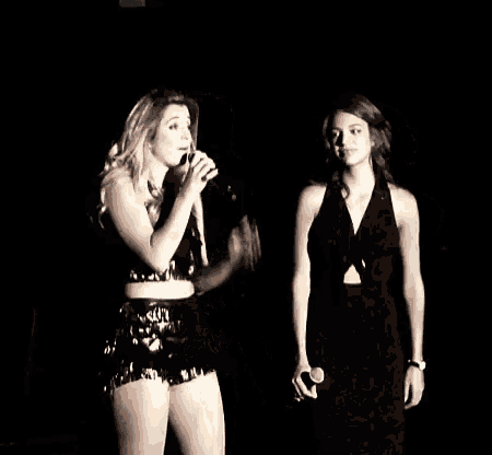 two women are standing next to each other on a stage in a dark room .