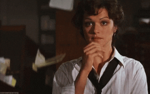 a woman in a striped shirt and tie is looking at the camera with her hands folded .