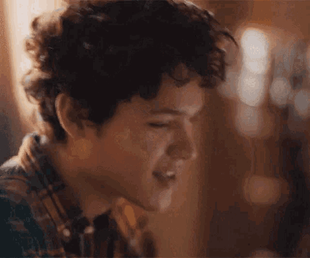 a young man with curly hair is smiling with his eyes closed in a close up .