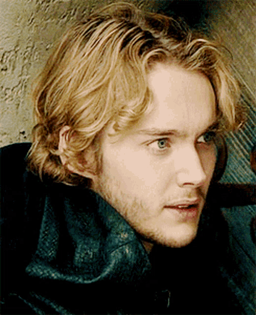 a young man with blonde hair and a beard looks at the camera
