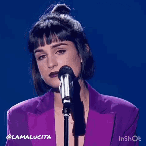 a woman in a purple suit is singing into a microphone .