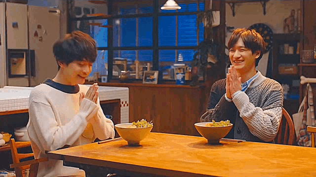 two men are sitting at a table with bowls of food on it