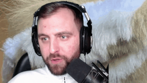 a man with a beard wearing headphones and a microphone looks at the camera