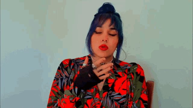 a woman with blue hair is smoking a cigarette while wearing a red and green shirt .