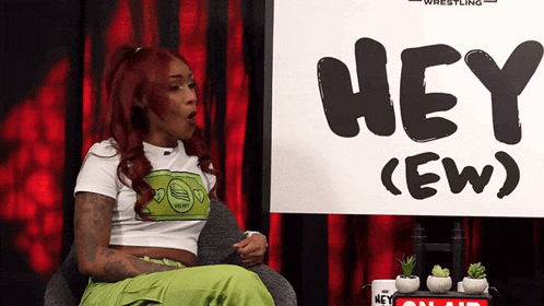a woman sitting in front of a sign that says hey