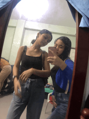 two girls are taking a selfie in a mirror