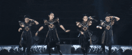 a group of women are dancing on a stage and one of them is holding a microphone