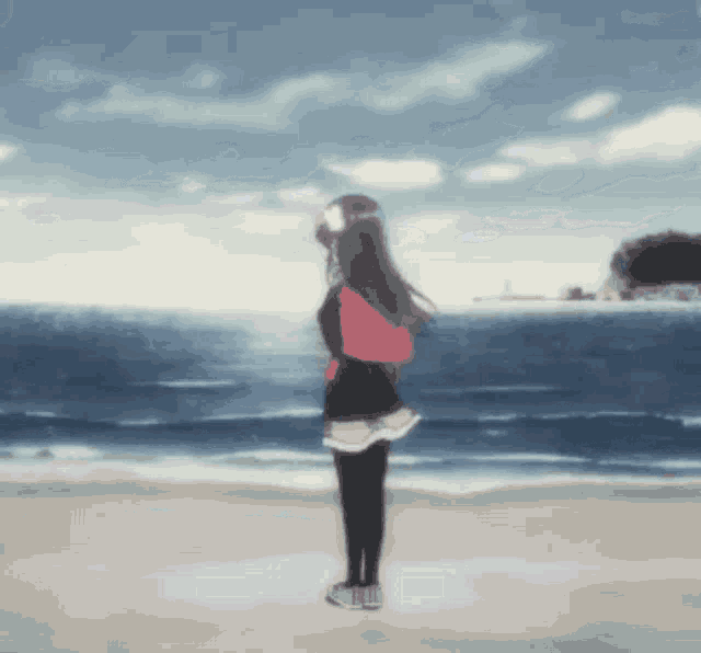 a girl standing on a beach with a red backpack