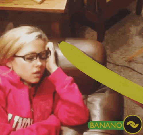 a girl wearing glasses sits on a couch next to a banana that says banano