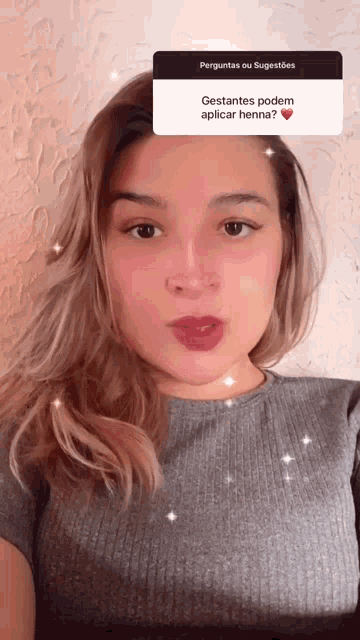 a woman wearing a grey shirt has a question about henna on her face