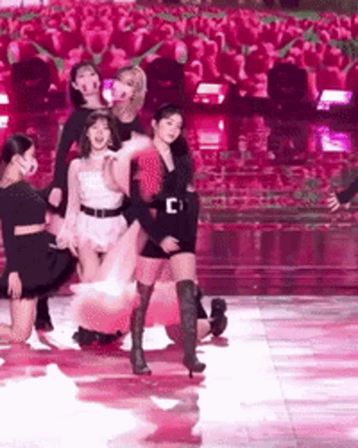 a group of women are dancing on a stage with a crowd in the background .