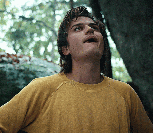 a man in a yellow sweater is looking up at something