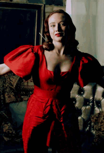 a woman in a red dress with puffed sleeves is standing in front of a couch