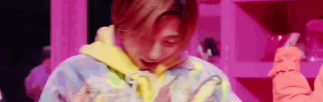 a close up of a person 's face with a pink background and a yellow hoodie .