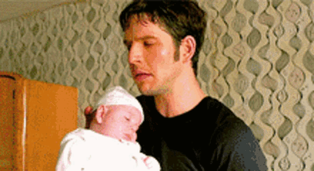 a man is holding a baby in his arms in front of a wall .