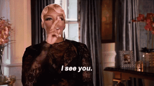 a woman in a black lace dress is standing in front of a window and says `` i see you '' .