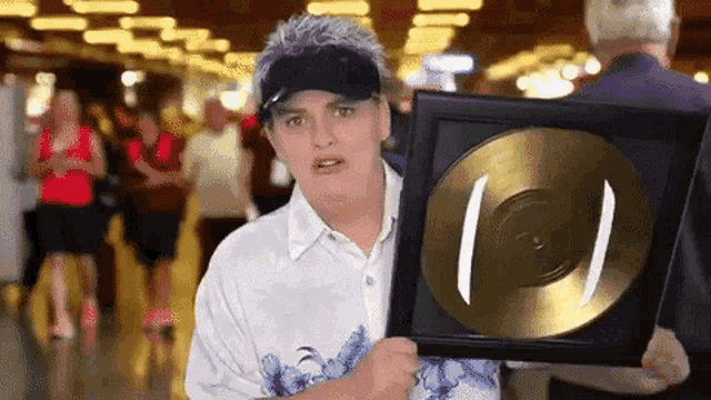 a woman wearing a visor holds a framed gold record