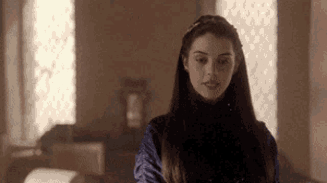 a woman with long hair is standing in front of a window in a room .