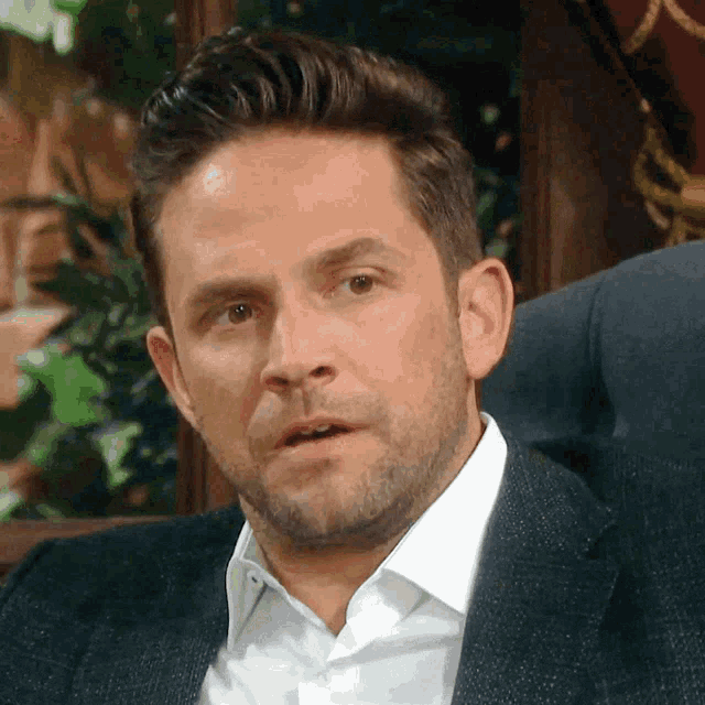 a man in a suit and white shirt is sitting in a chair and making a funny face