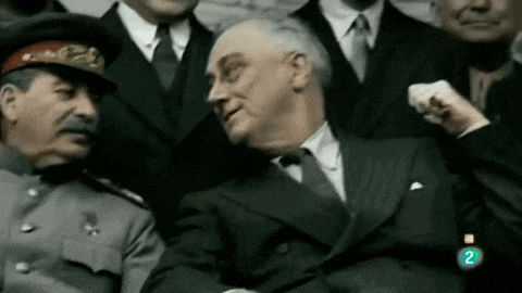 a man in a suit is sitting next to a man in a hat with the number 2 on the bottom right