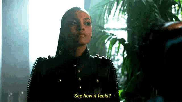 a woman in a black leather jacket is standing in front of a plant and talking to someone .