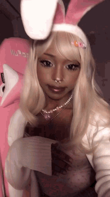a woman wearing a pink bunny headband and a white sweater is taking a selfie .