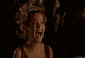 a woman is smiling in a dark room while holding a cigarette .