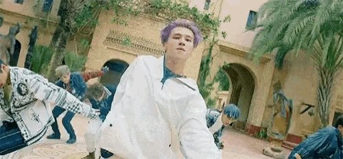 a man with purple hair is standing in front of a group of people .