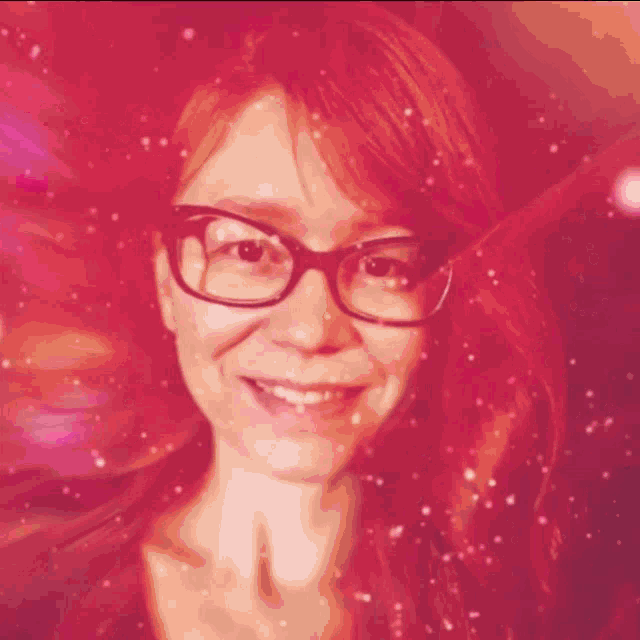 a woman with red hair and glasses smiles in a pink background
