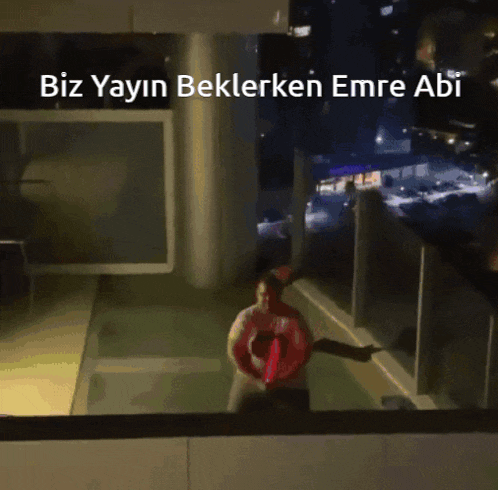 a man in a life preserver stands on a balcony with the words biz yayin beklerken emre abi