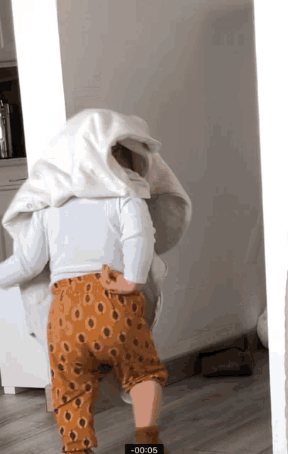 a baby with a white blanket on his head is walking