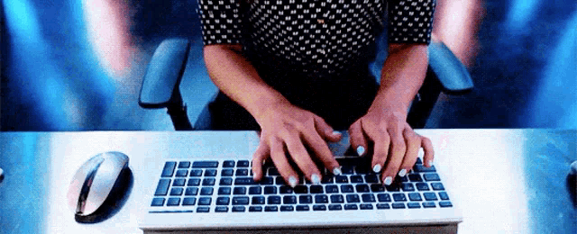 a woman is typing on a computer keyboard with a mouse nearby
