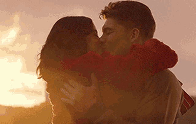 a man and woman are kissing each other in front of a sunset .