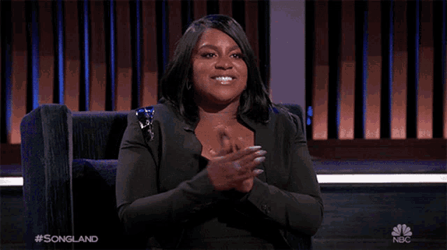 a woman applauds while sitting in a chair with the nbc logo in the background