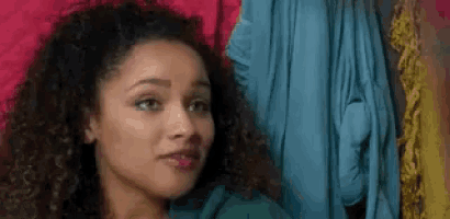 a woman with curly hair is looking at the camera while standing in front of a closet .