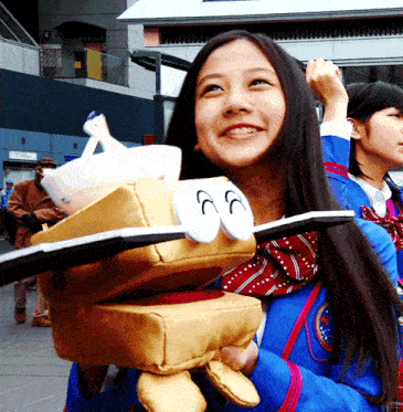 a girl in a blue jacket is holding a stuffed animal with the letters cc on its face