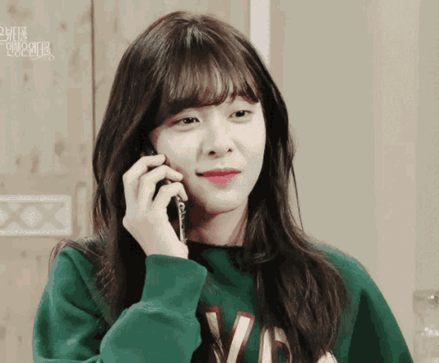 a woman wearing a green sweatshirt with the letter v on it talking on a cell phone