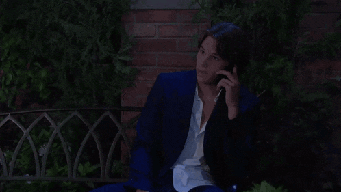 a man in a suit is talking on a cell phone while sitting in a chair .