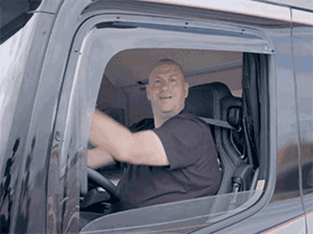 a man is sitting in the driver 's seat of a truck and smiling .