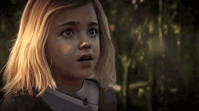 a little girl with blonde hair and blue eyes is looking at the camera with a surprised look on her face