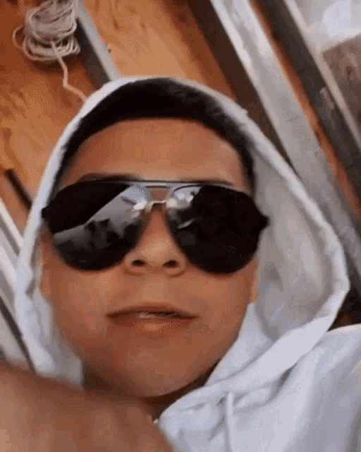 a young man wearing sunglasses and a white hoodie is giving a thumbs up .