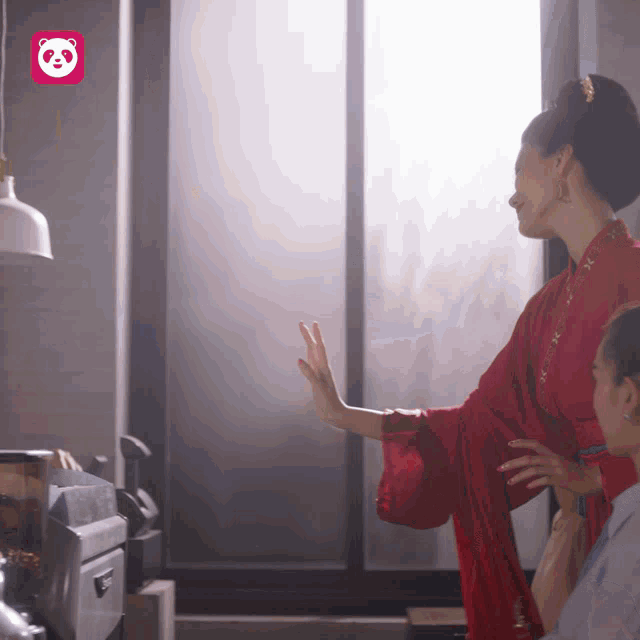 a woman in a red dress is standing in front of a window