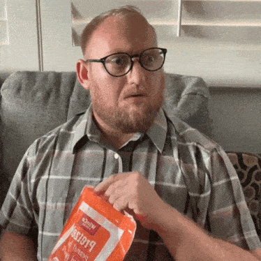 a man wearing glasses is holding a bag of chips that says mac n cheese on it