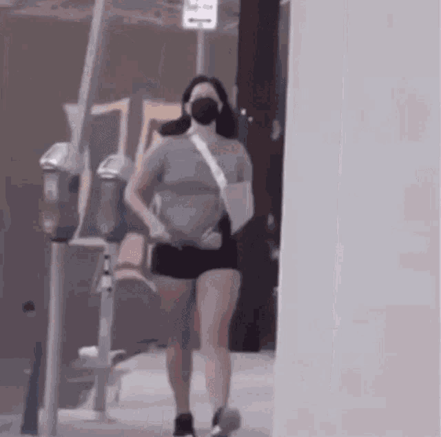 a woman wearing a mask and shorts is walking down a street .