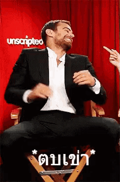 a man in a suit is sitting in a chair with his legs crossed and laughing