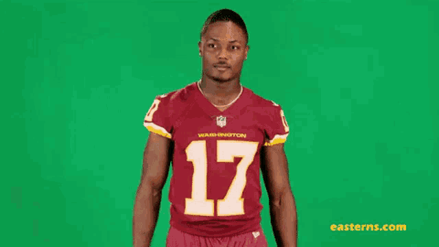 a man in a washington redskins jersey is standing in front of a green background .