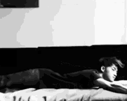 a black and white photo of a man laying on his stomach on a bed .