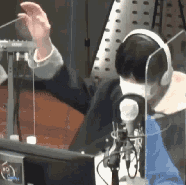 a man wearing headphones and a mask is sitting in front of a microphone in front of a computer .