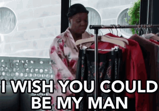 a woman in a robe is standing in front of a rack of clothes and says " i wish you could be my man "