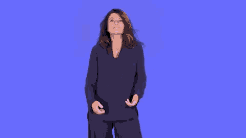 a woman in a black top and black pants is standing in front of a blue background